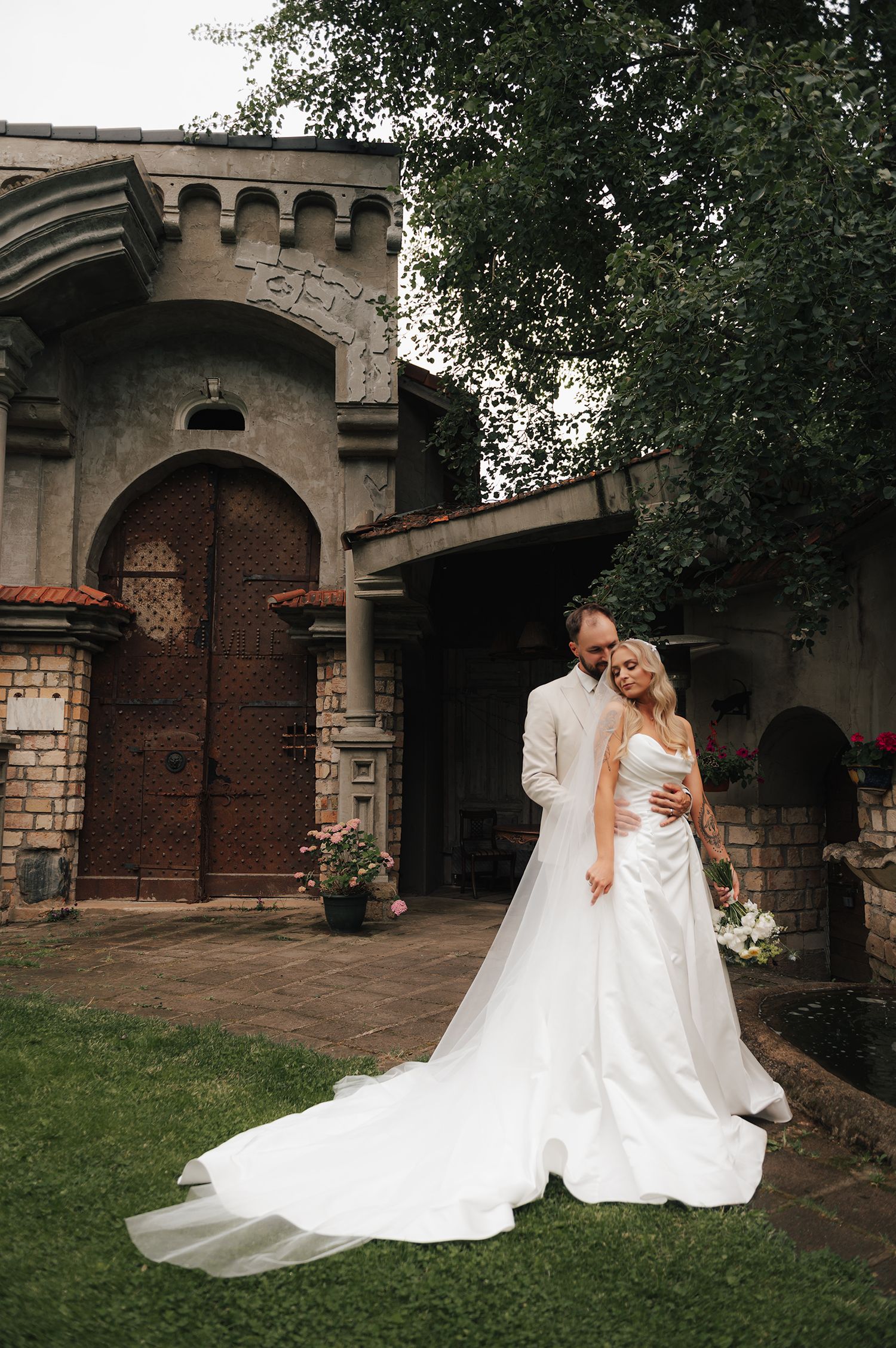 A couple in wedding attire share romantic moments in front of a rustic stone church with wooden doors and arches.