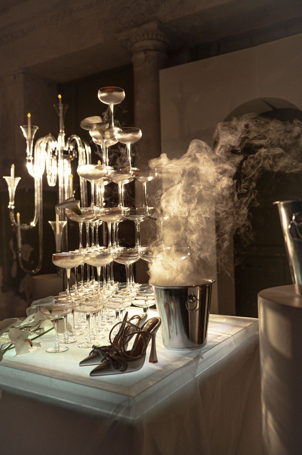 Elegant champagne tower with crystal glasses, high heels, and a smoking silver ice bucket at a luxury event.
