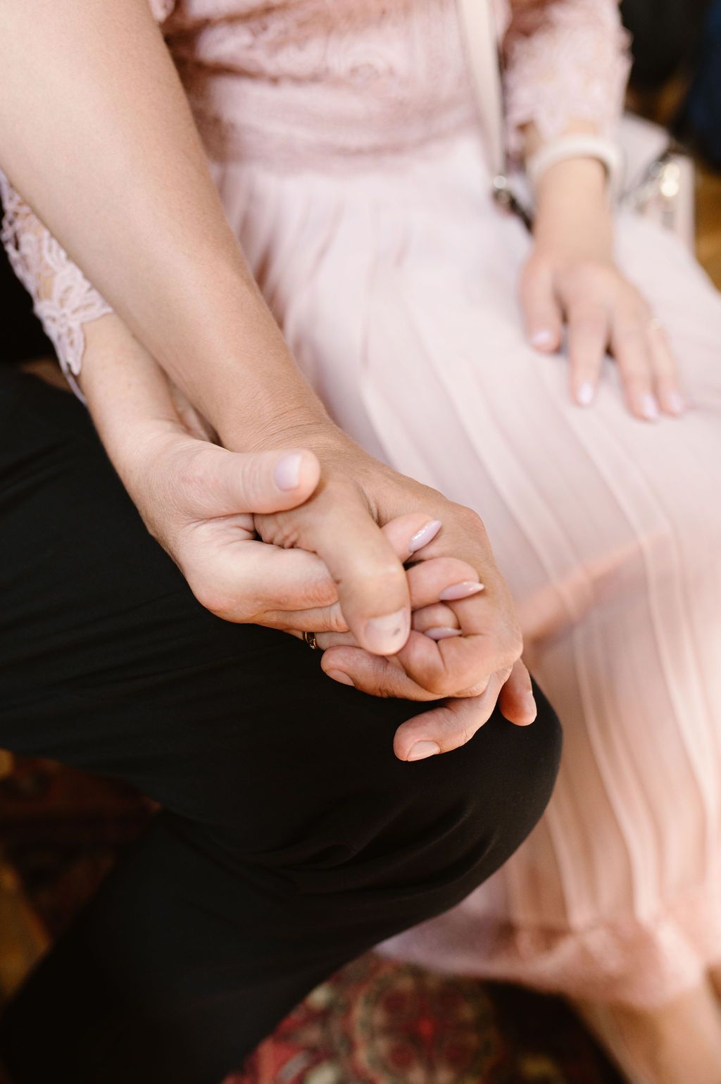 Close-up of a couple holding hands, woman in pink dress and man in black pants, suggesting a romantic wedding moment.
