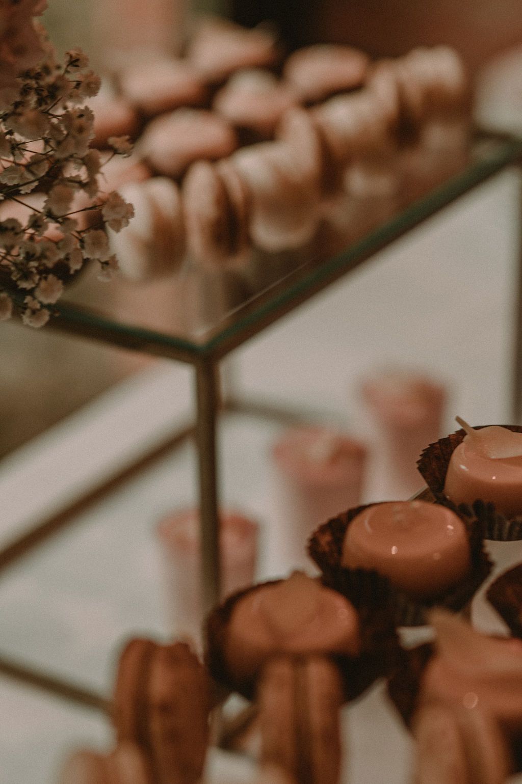 Elegant dessert display with pink macarons and chocolate-dipped treats on a glass tiered stand at a wedding reception.