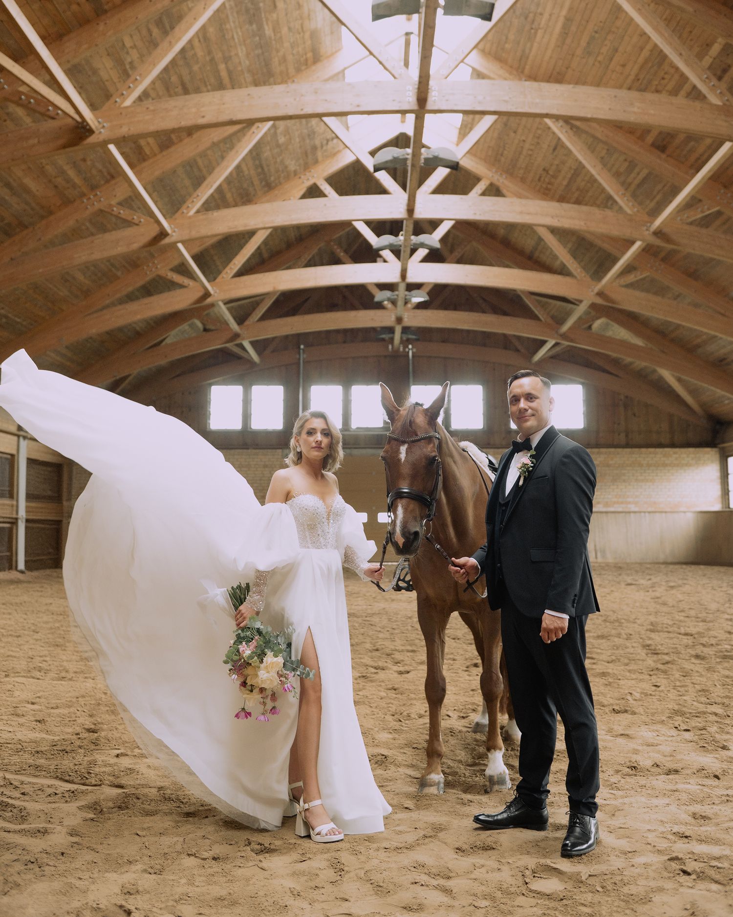 A flowing white wedding dress twirls gracefully inside a rustic wooden barn with exposed beams and sandy floor.