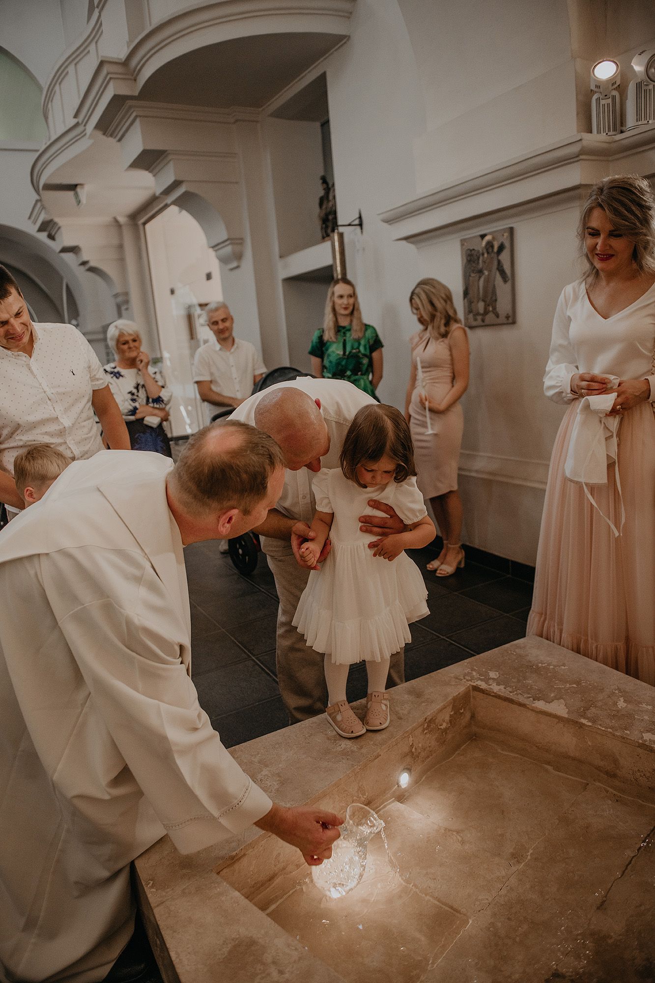 A baptism ceremony takes place in a church as people gather around the baptismal font during a special moment.