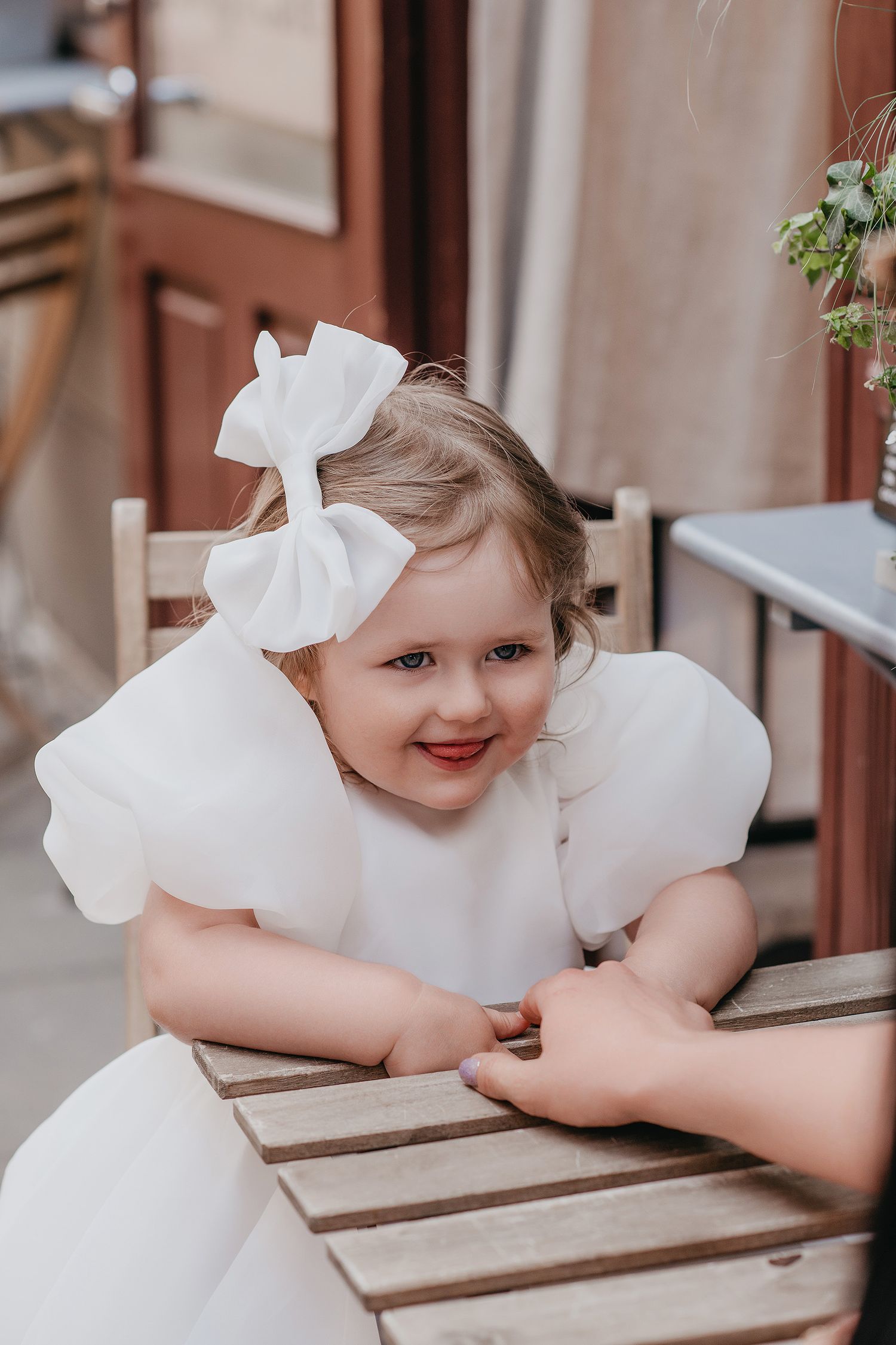 A child in a white dress with bows leans on a wooden surface in a sequence of similar poses.