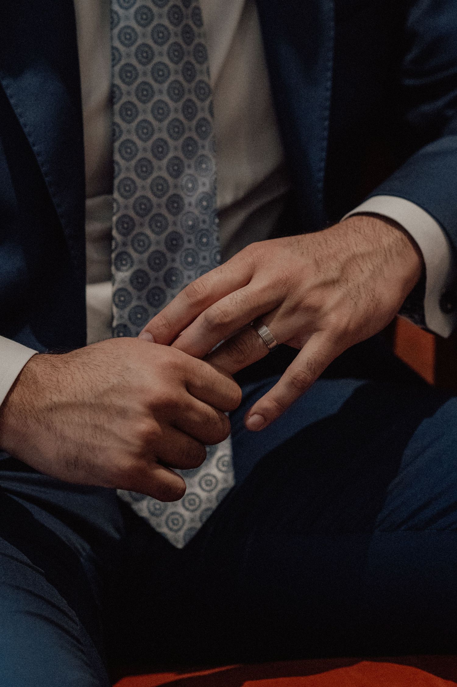 Close-up of hands adjusting a patterned blue necktie against a dark suit.
