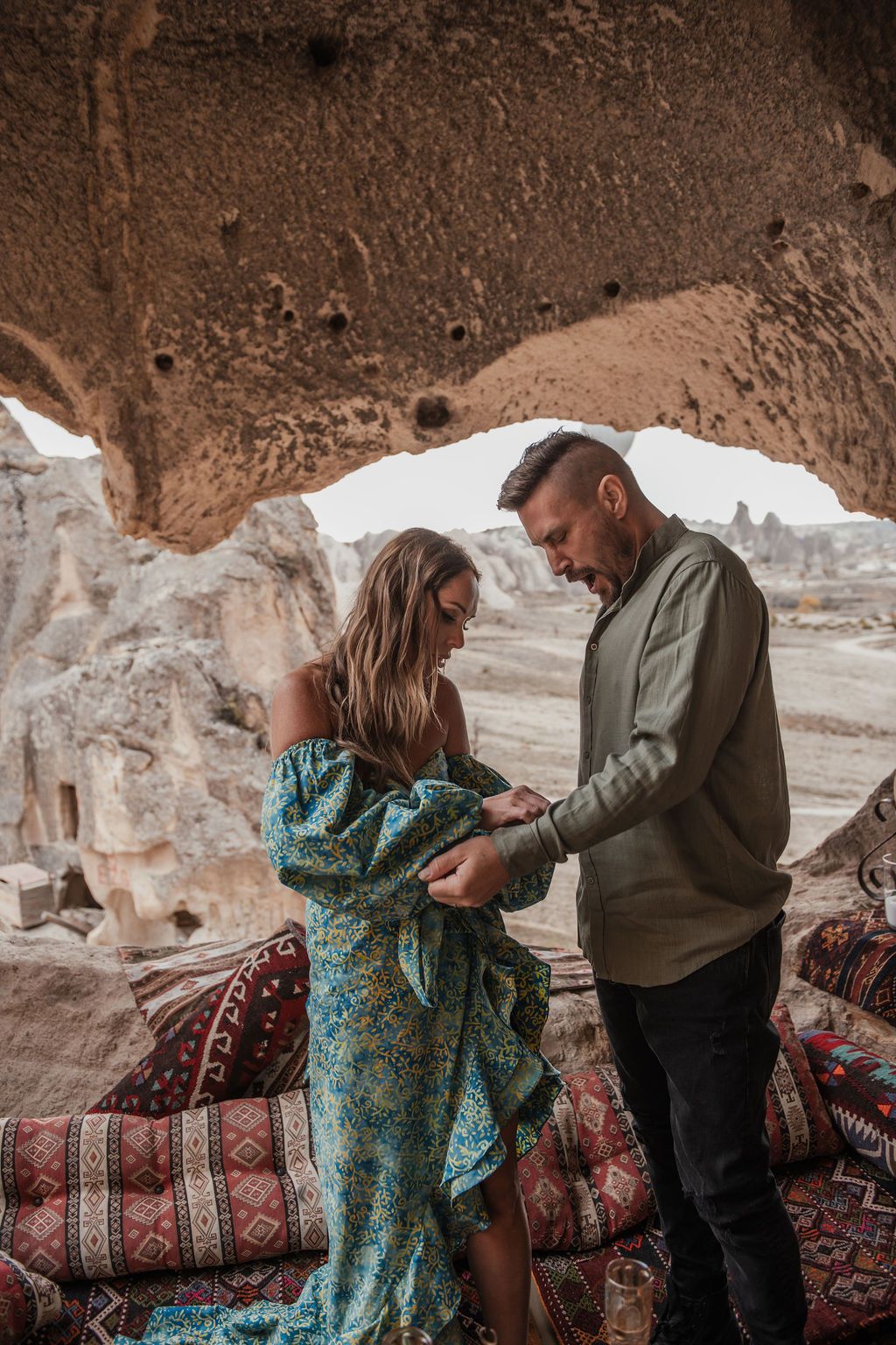 Couple sharing a romantic moment in a cave dwelling in Cappadocia, Turkey, surrounded by colorful rugs and rock formations.