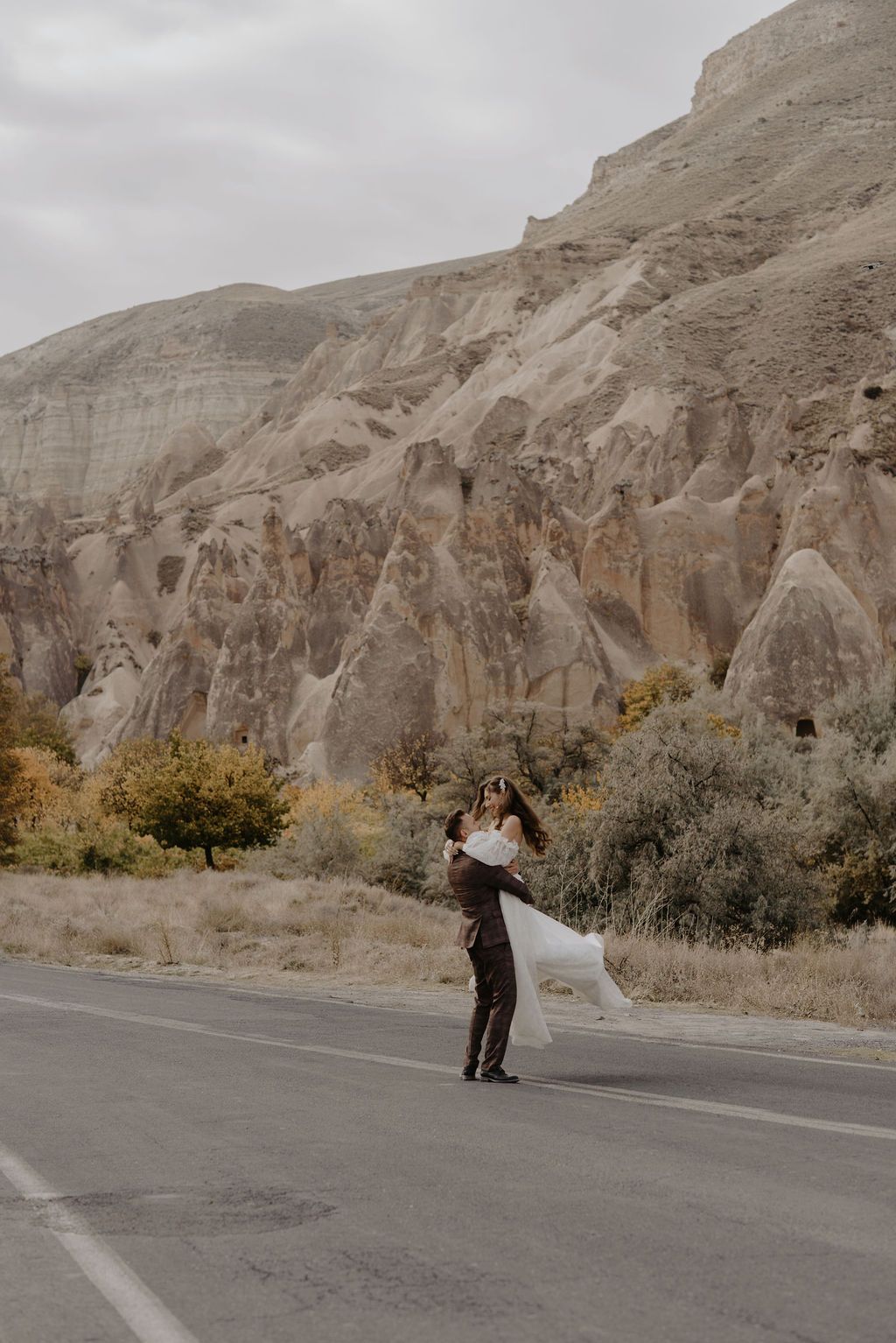 Groom lifting bride in white dress near stunning rock formations in Cappadocia, Turkey.