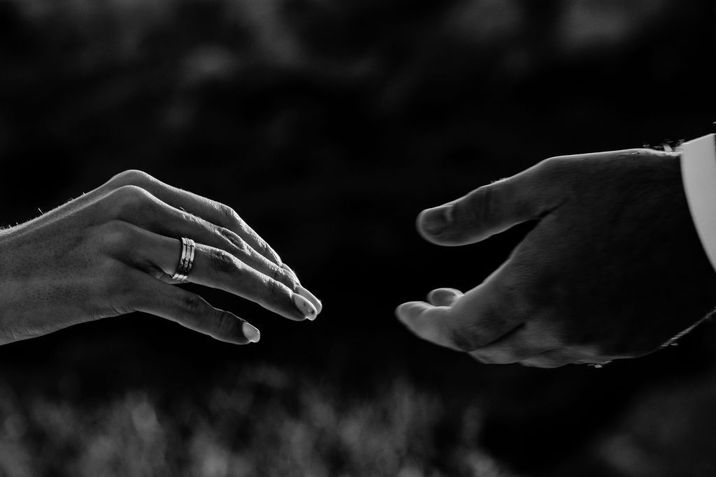 Black and white close-up of two hands reaching toward each other, woman wearing a diamond engagement ring.