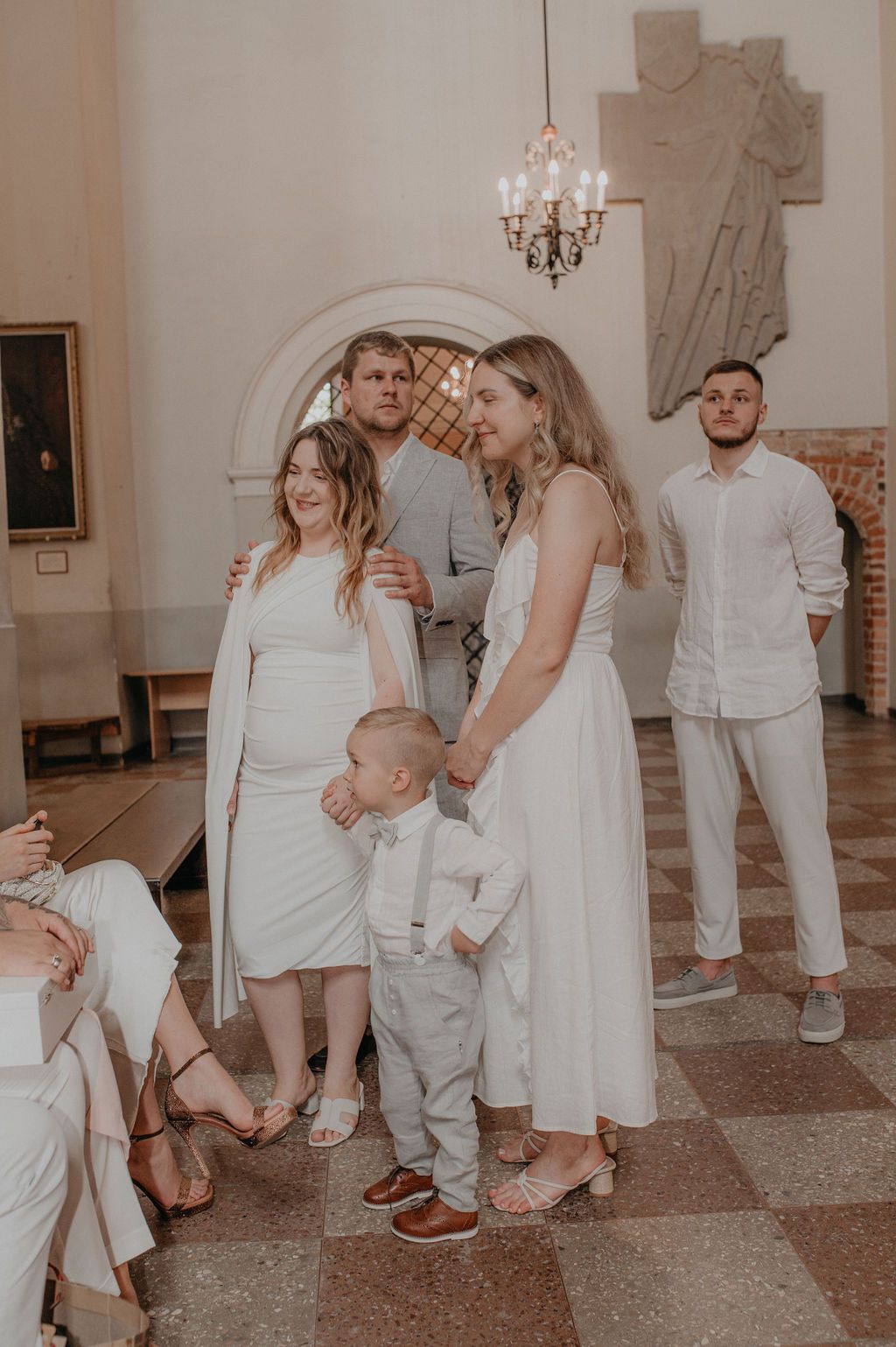 Family dressed in white attire posing together in an elegant church interior during a wedding ceremony.