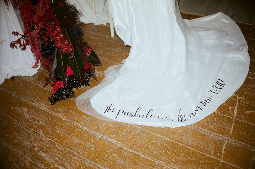 White wedding dress train with calligraphy script writing on floor beside red floral arrangement.