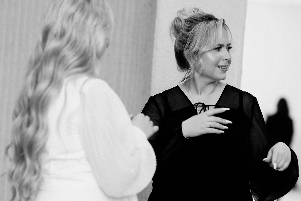 Black and white photo of two women in elegant attire sharing a joyful moment at a formal event.