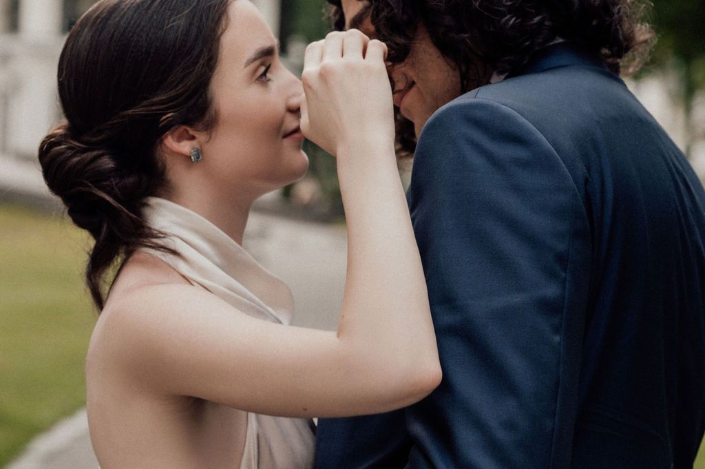A bride and groom share an intimate moment, smiling closely as she gently touches his face during their wedding day.