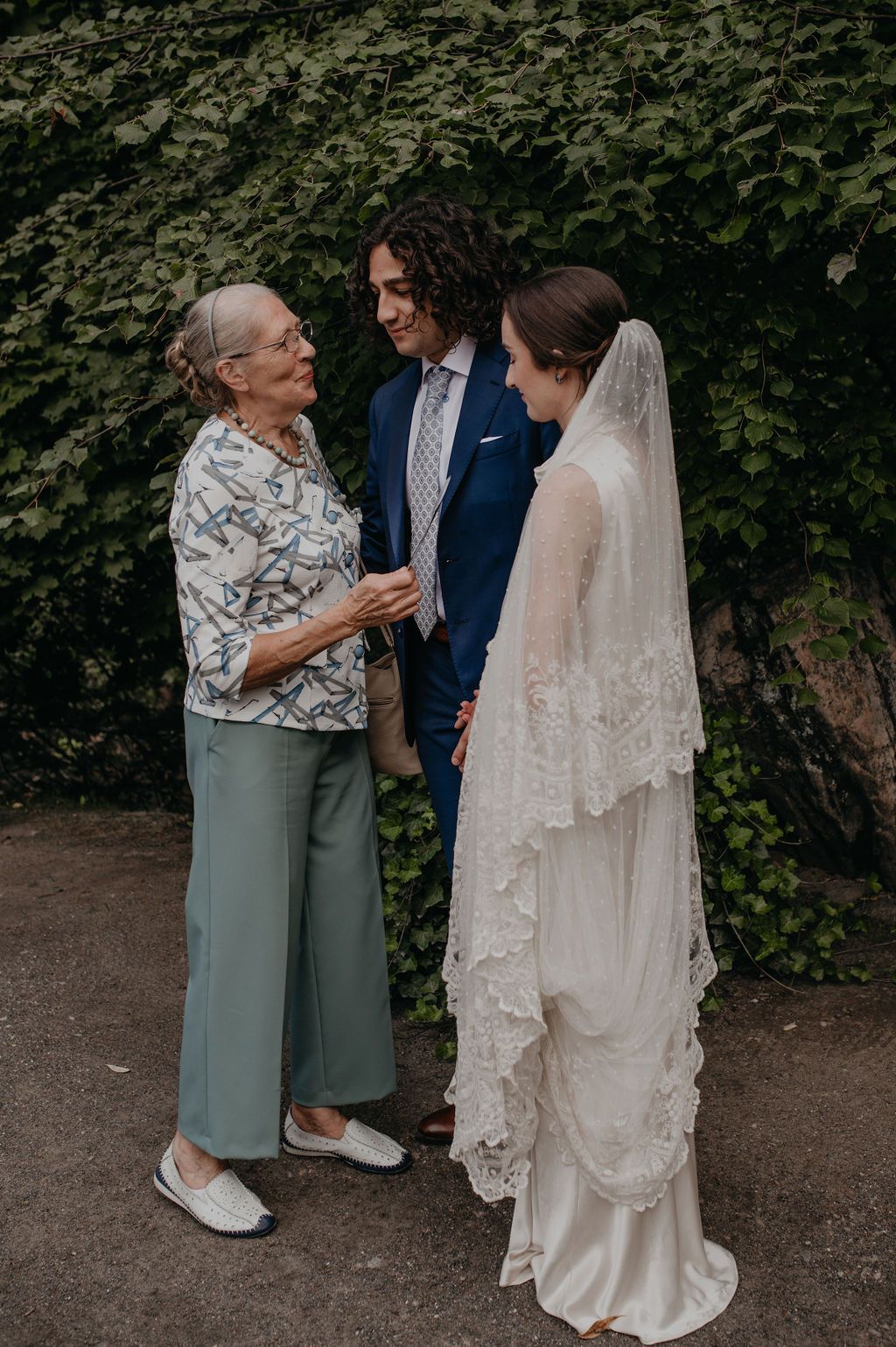 Elderly woman congratulating bride and groom in blue suit at outdoor wedding reception.