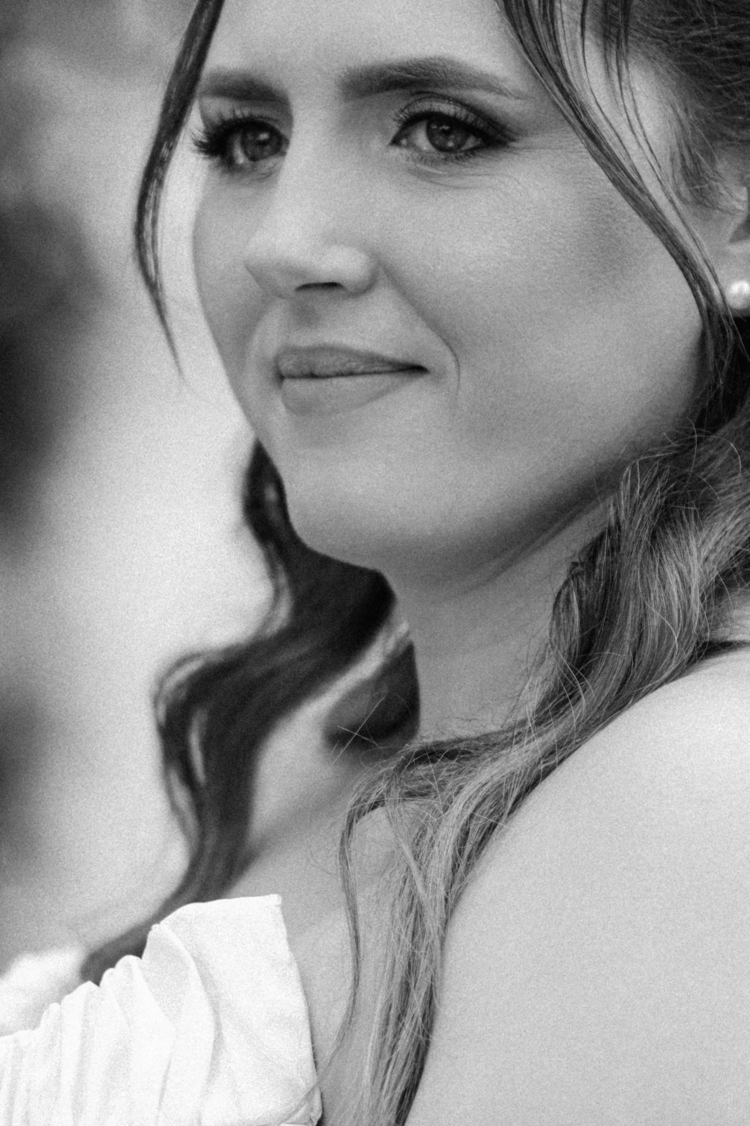 Black and white portrait of a young woman with wavy hair, wearing a white off-shoulder top, smiling softly.