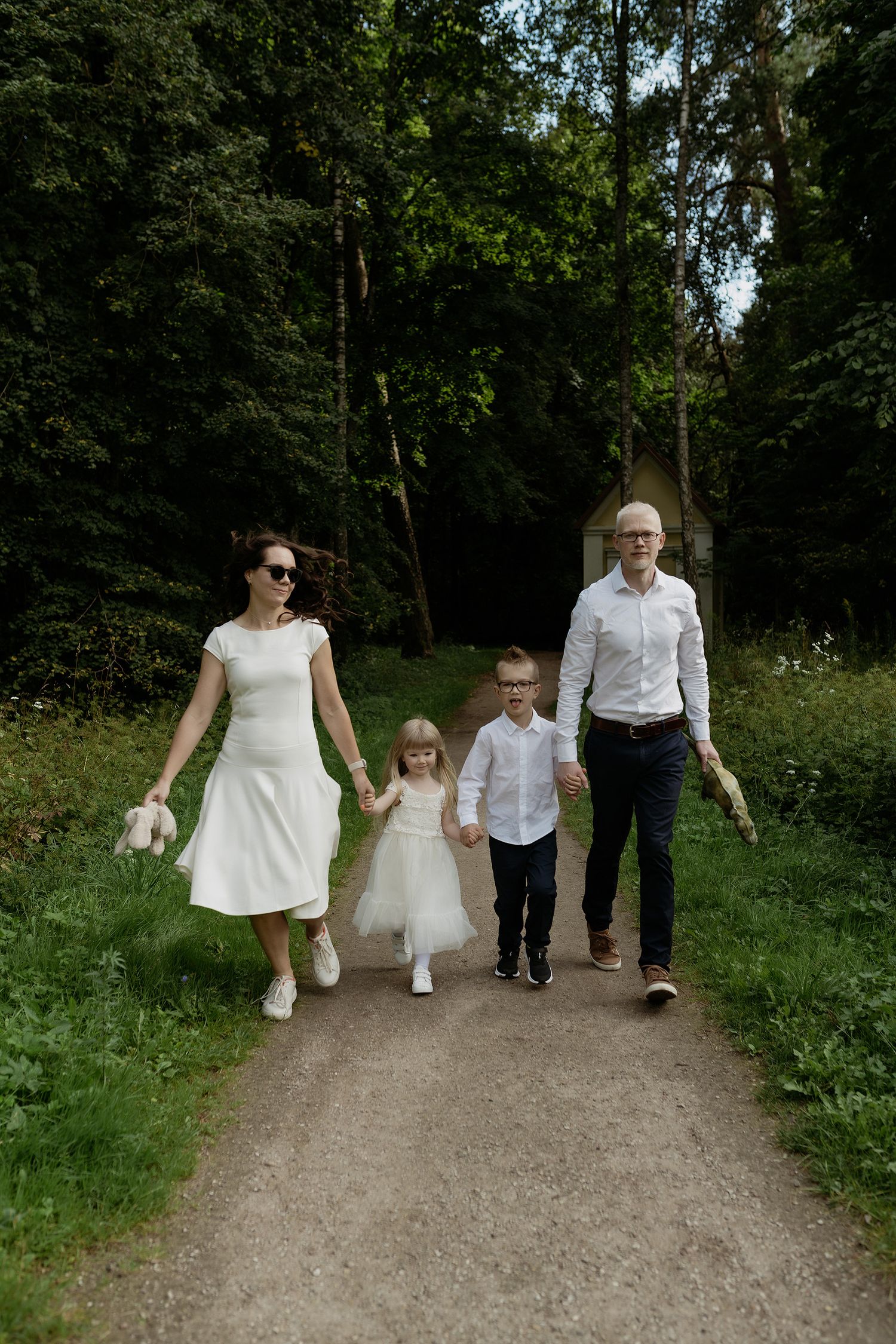 A family walks together on a dirt path through a lush green forest on a summer day.