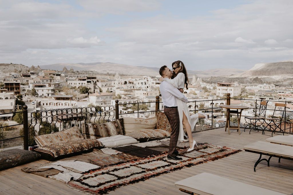 Couple embracing on a rooftop terrace with panoramic views of a Middle Eastern city landscape.