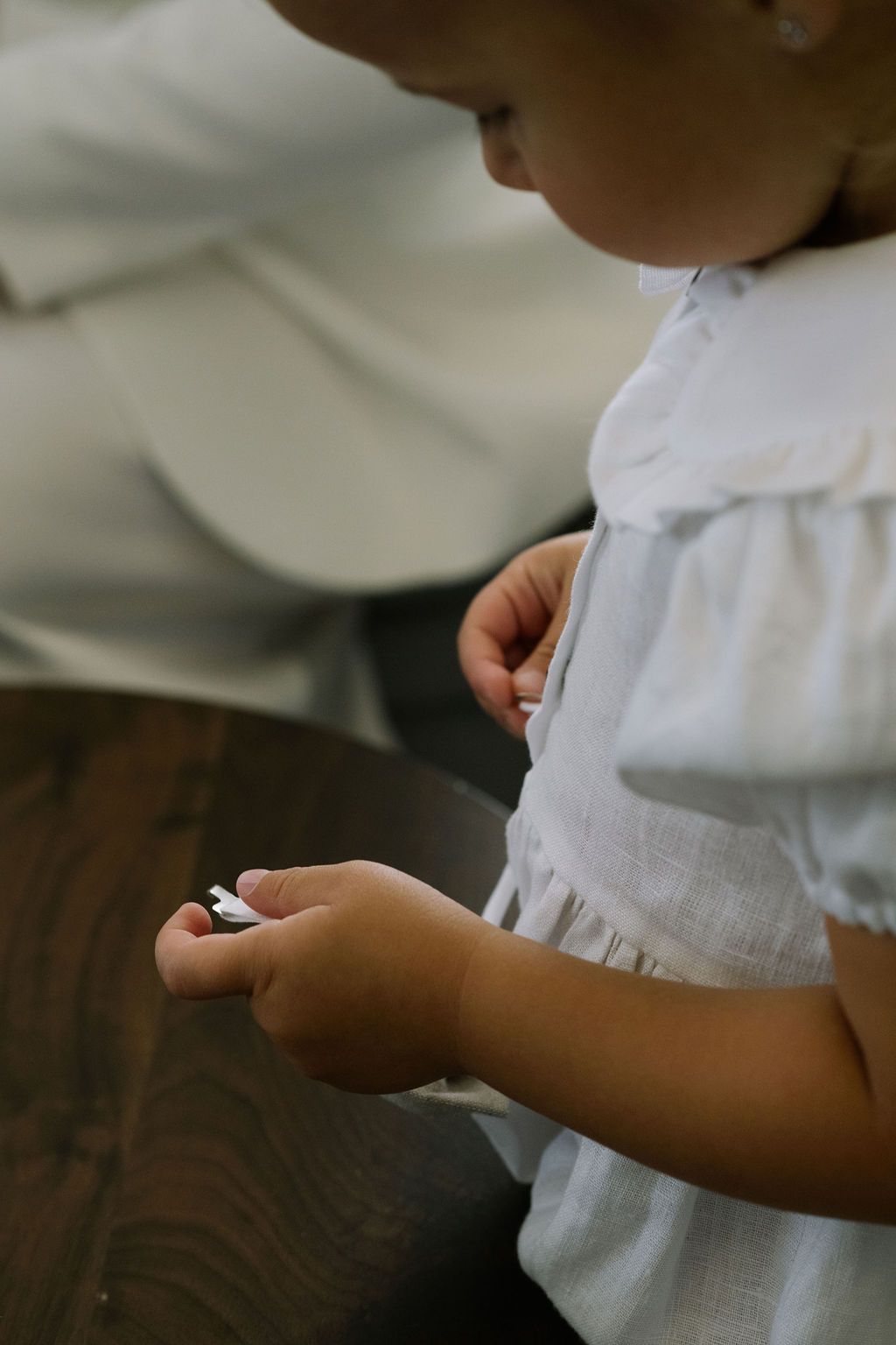 Young girl in white dress carefully holding a small white object in her hands while seated indoors.