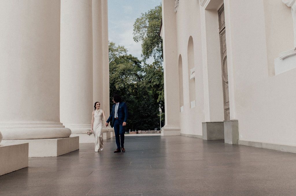 Elegant couple walking between grand white columns at a classical building, perfect for wedding photography.