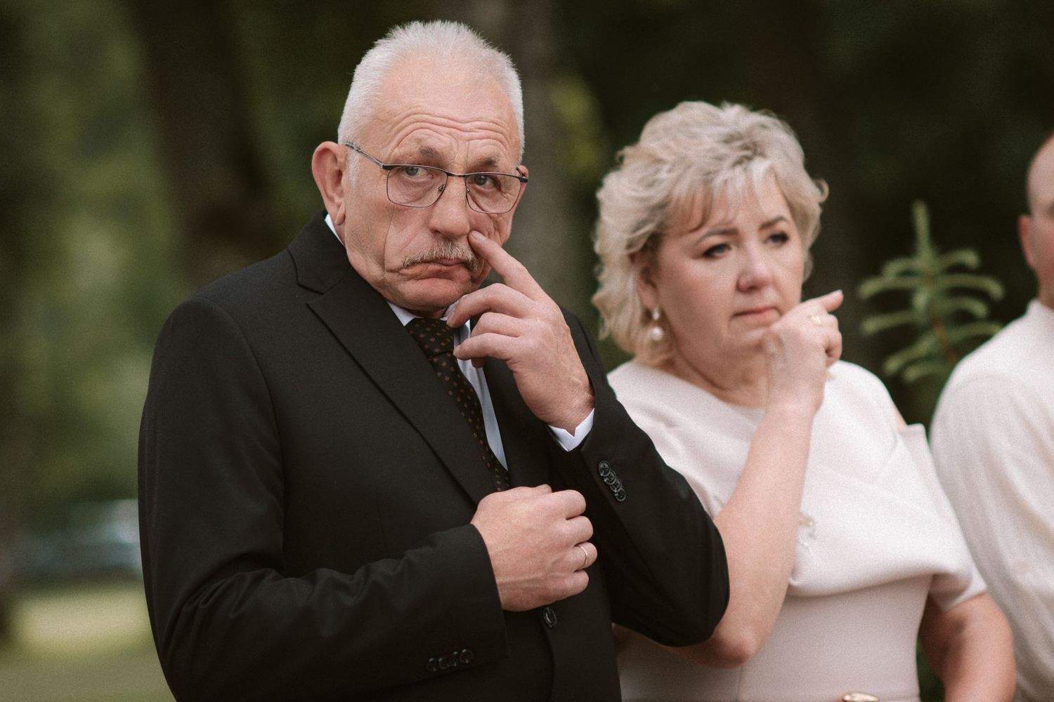 Elderly couple in formal attire looking thoughtful at an outdoor wedding ceremony.