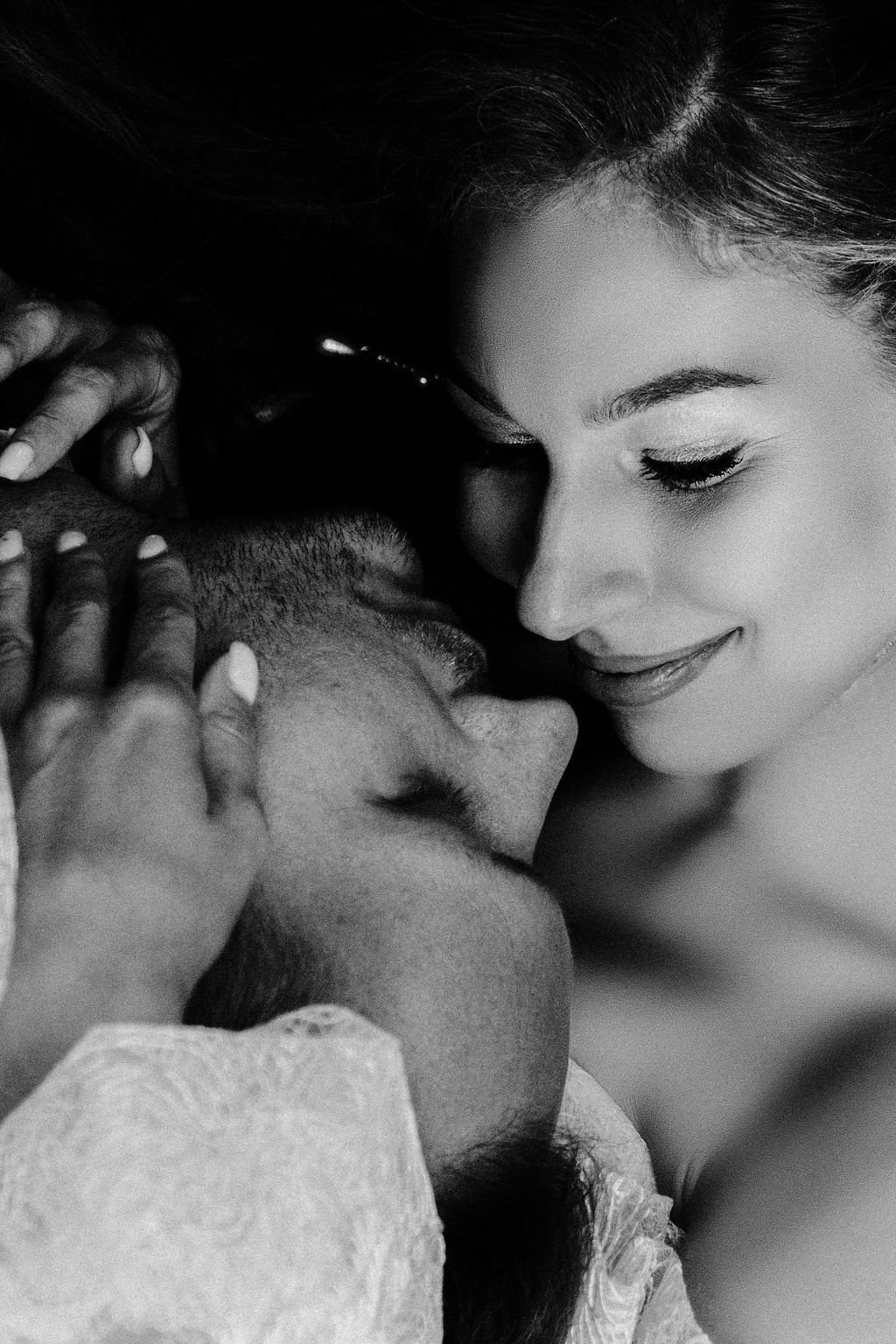 Black and white photo of a smiling bride tenderly holding her groom's face close to hers.