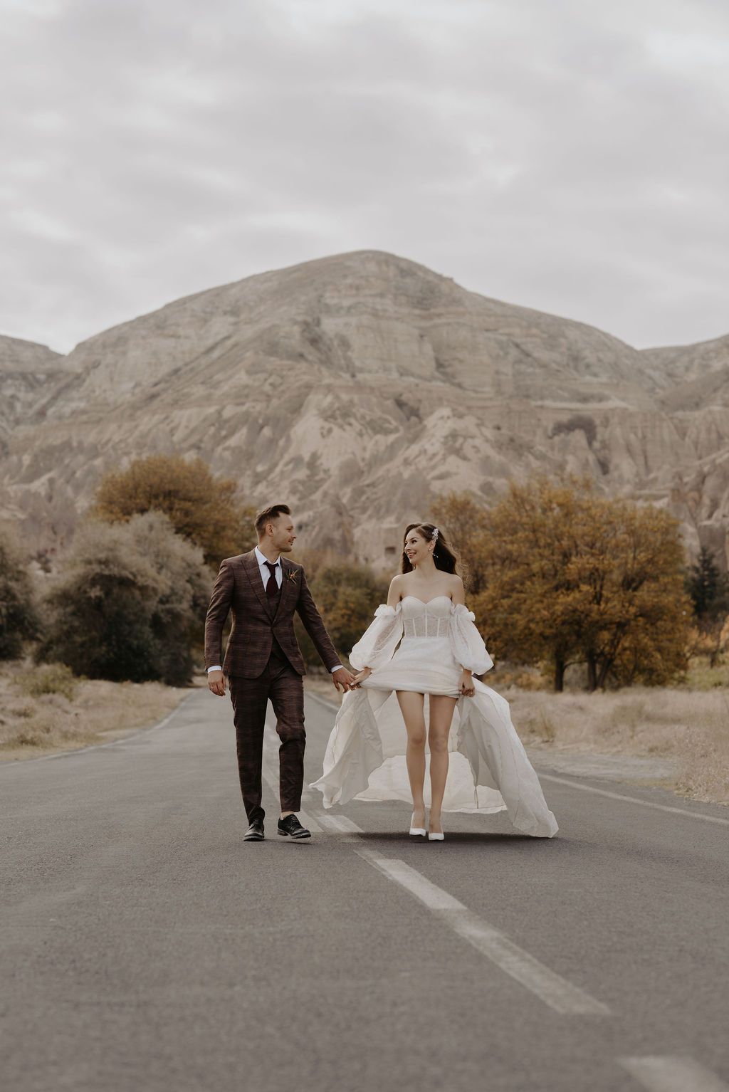 Wedding couple walking hand in hand on a road with dramatic rocky mountains in background.