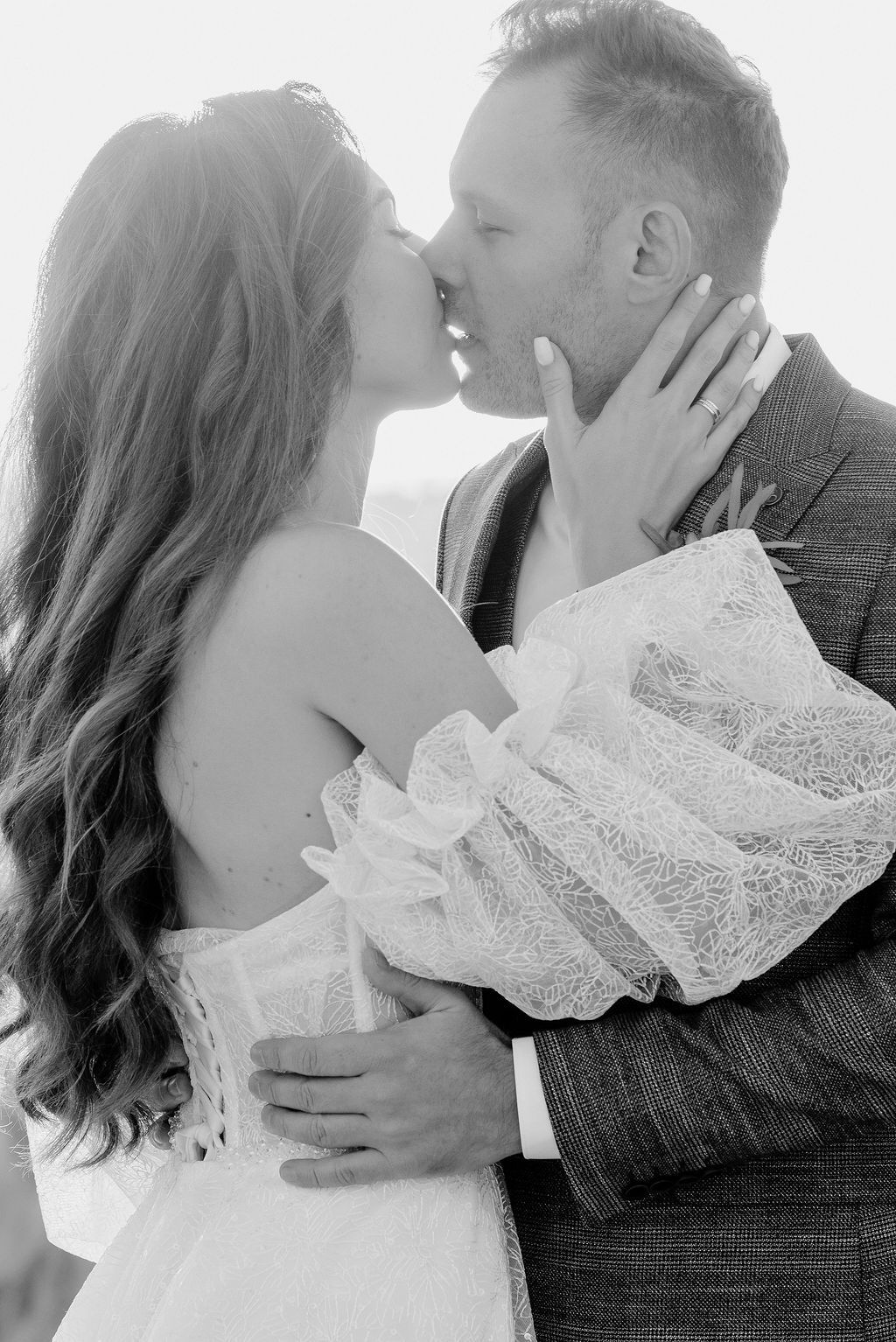 Black and white photo of bride and groom sharing a tender kiss in soft backlight.