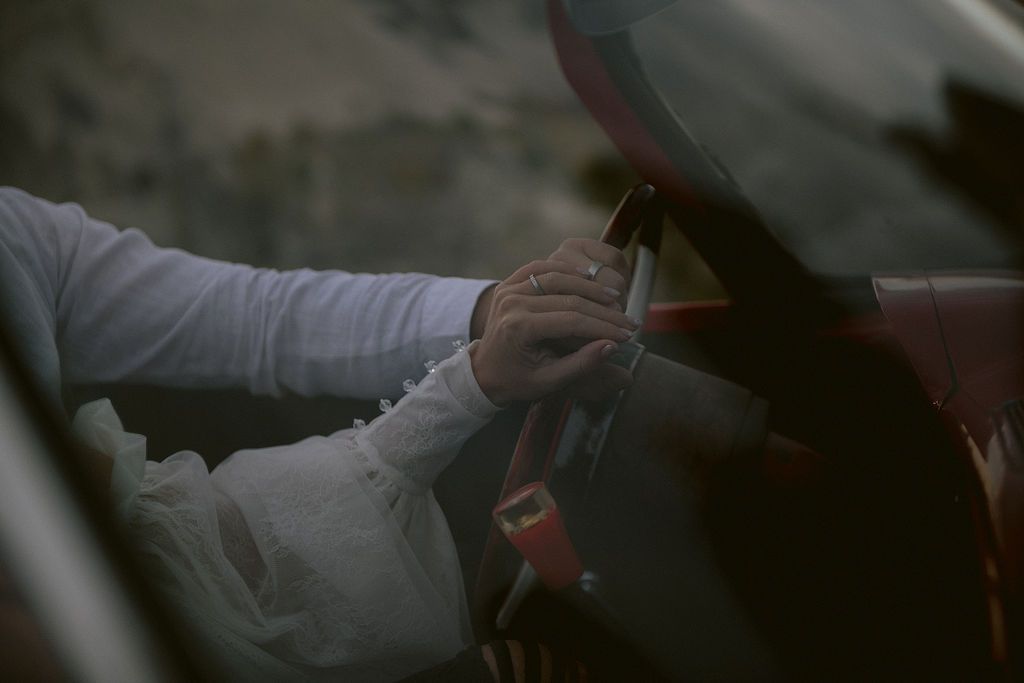 Close-up of a driver's hands gripping a red race car steering wheel wearing a white racing suit.