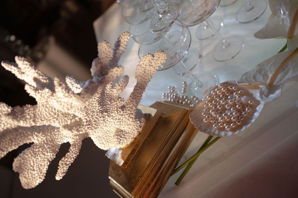 White coral sculpture and pearl decorations displayed alongside elegant glass stemware on a gold surface.