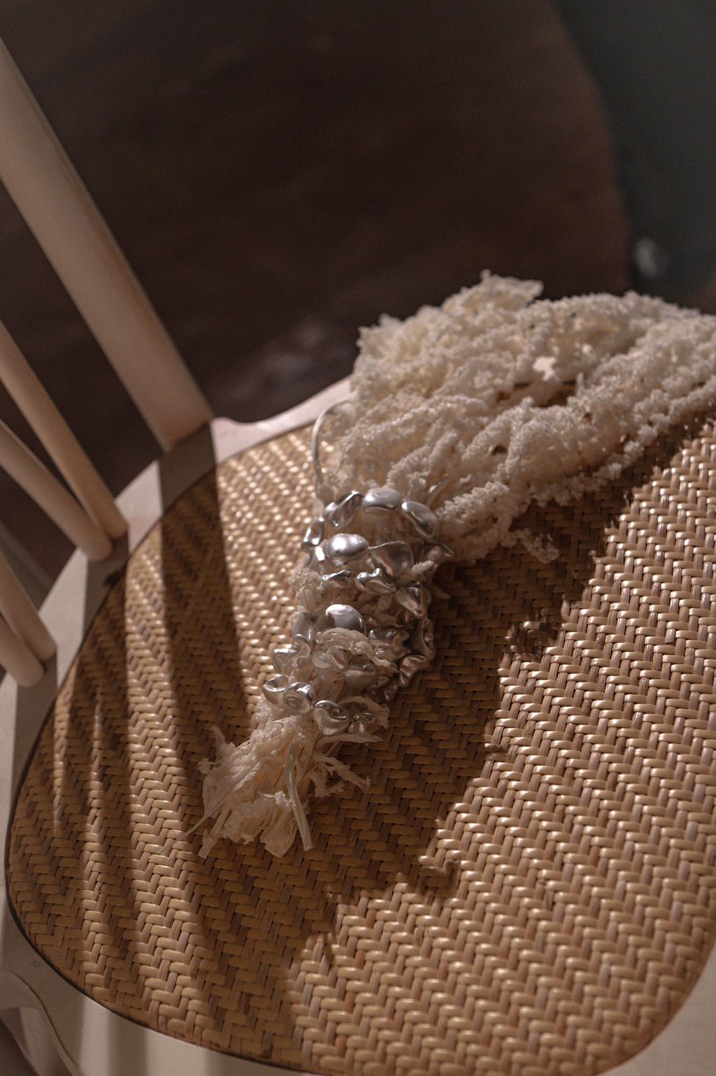 Delicate beaded bridal bracelet with silver accents resting on a woven rattan chair seat.