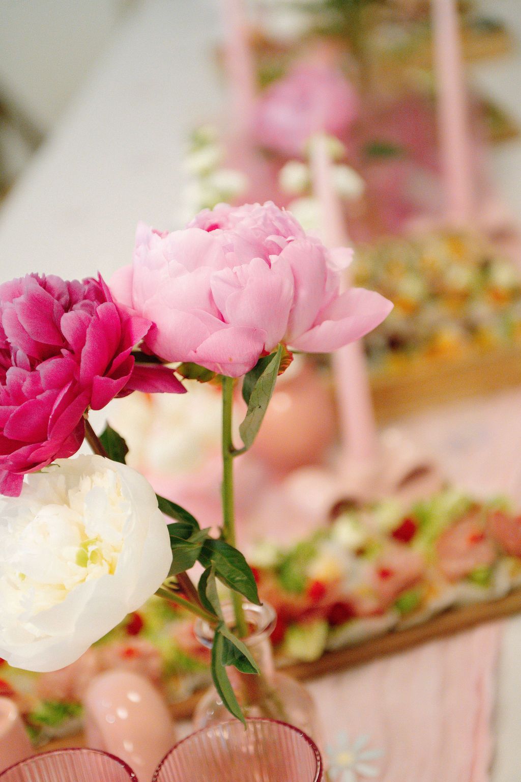 Pink, magenta, and white peonies arranged in vases on a decorated table with pastel accents.