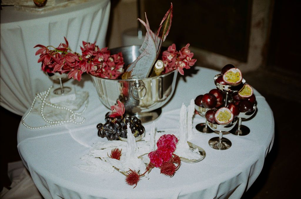 Elegant table display with red floral arrangements, pearl necklace, champagne bucket, and decorative dessert stands at a formal event.