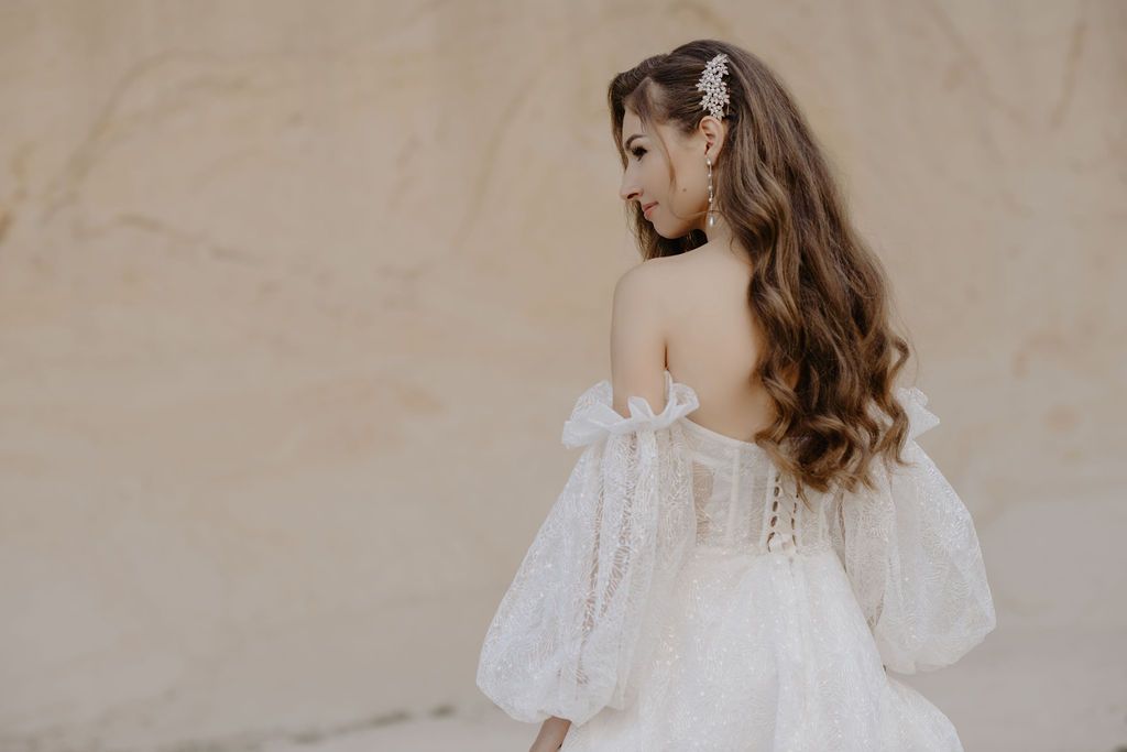 Bride with wavy hair in a strapless white gown with puff sleeves and floral hair accessory outdoors.