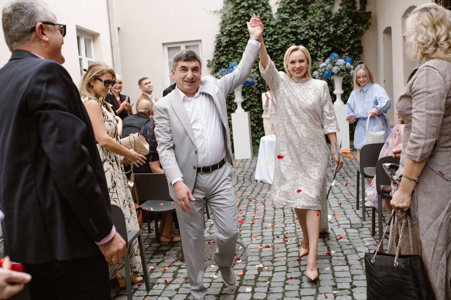Wedding guests throw confetti and celebrate on a cobblestone street outside a venue.