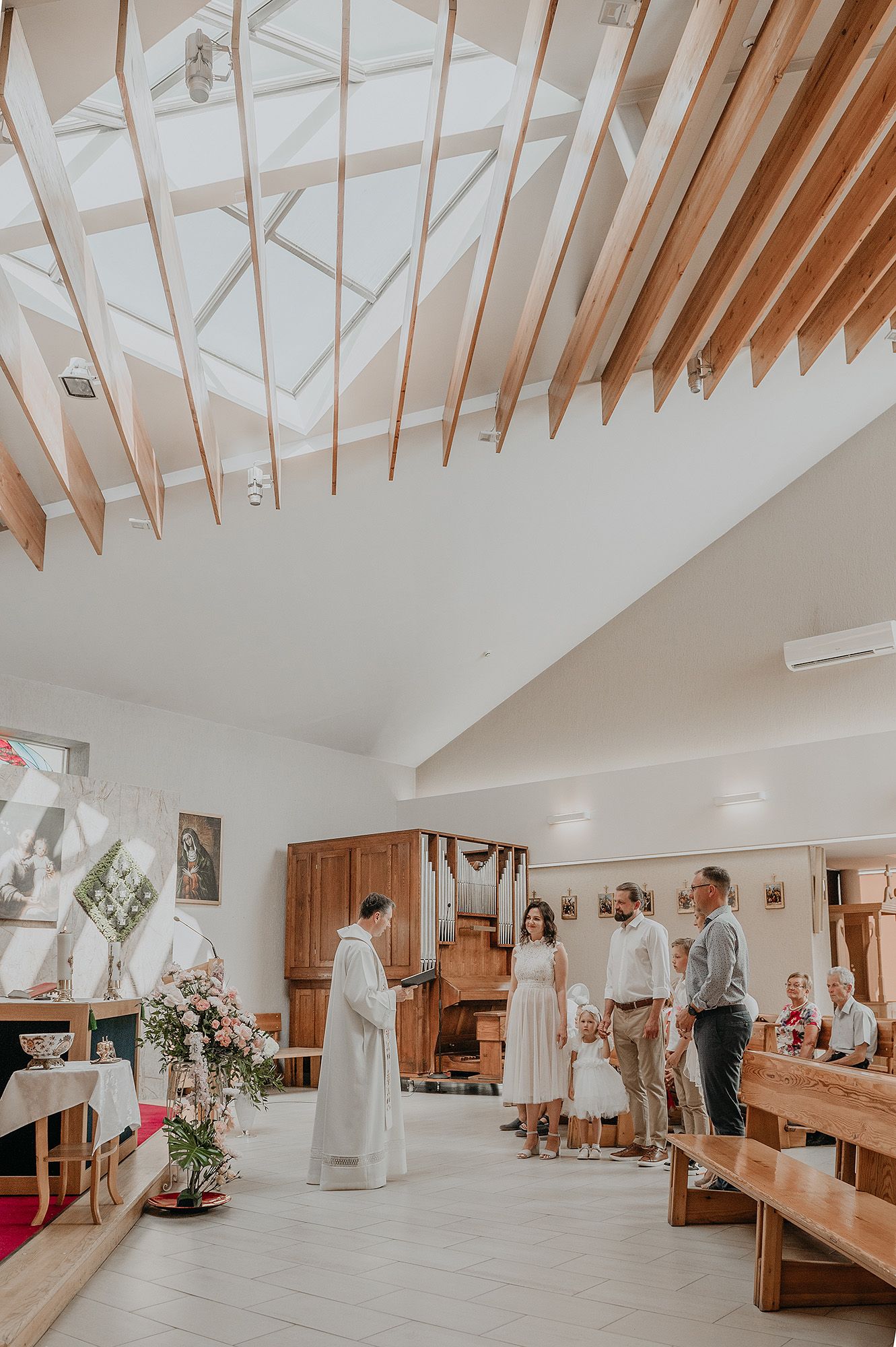 Interior of a bright white bridal boutique with wooden beams, clothing racks, and natural lighting from skylights.