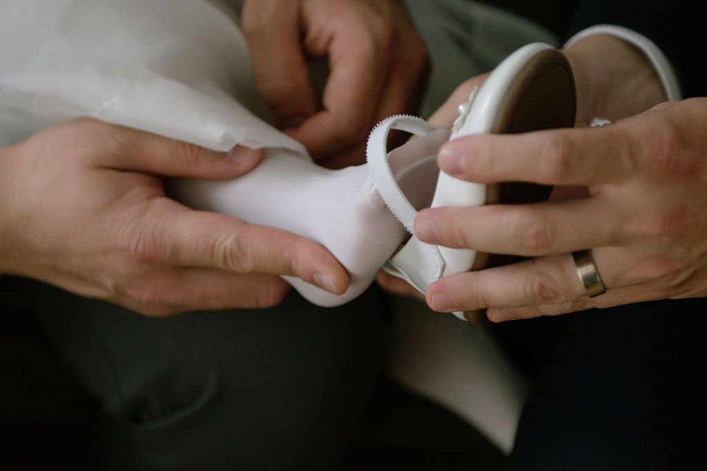 Hands with wedding ring helping bride put on white satin wedding shoe.
