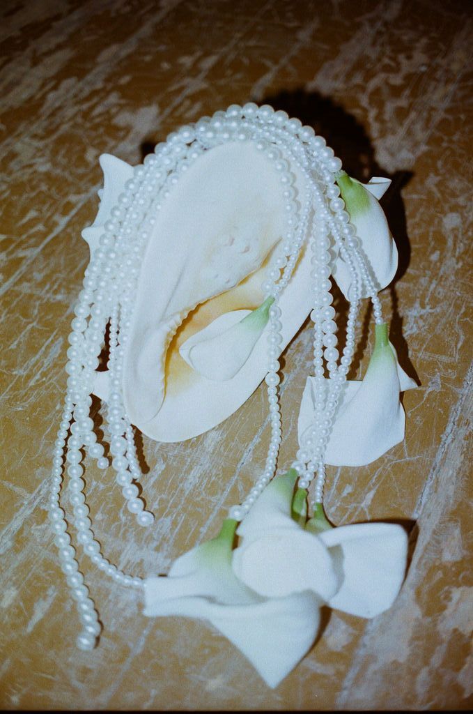 White calla lilies arranged with cascading pearl strands on a marble surface, elegant bridal accessory.