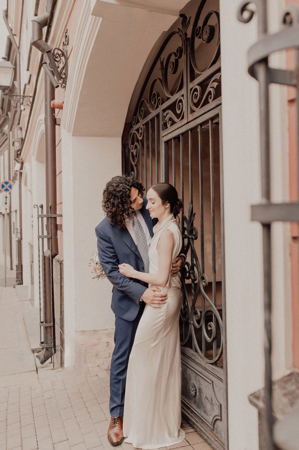Couple embracing in front of ornate iron gate during romantic urban wedding photo session.