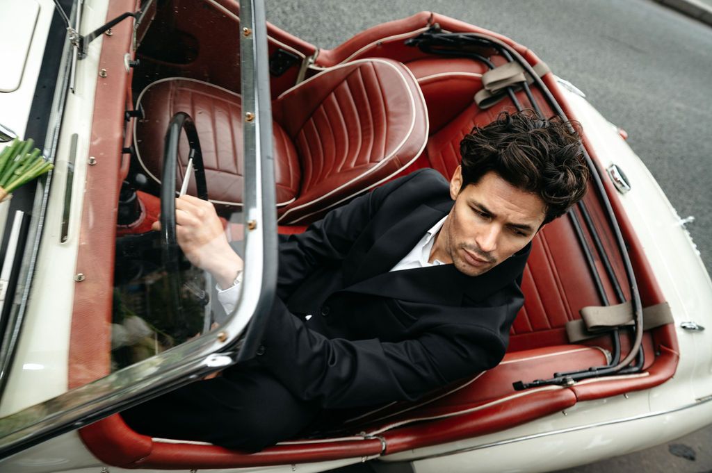 Stylish man in black suit sitting in a vintage red and white convertible car, shot from above.
