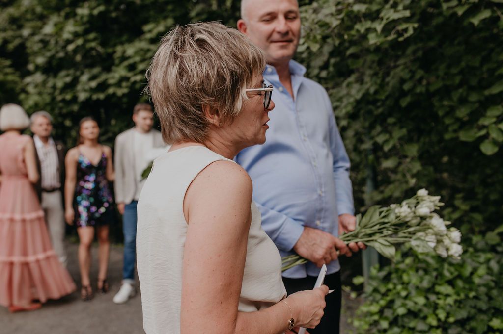 Woman holding white flowers at an outdoor wedding reception surrounded by guests.