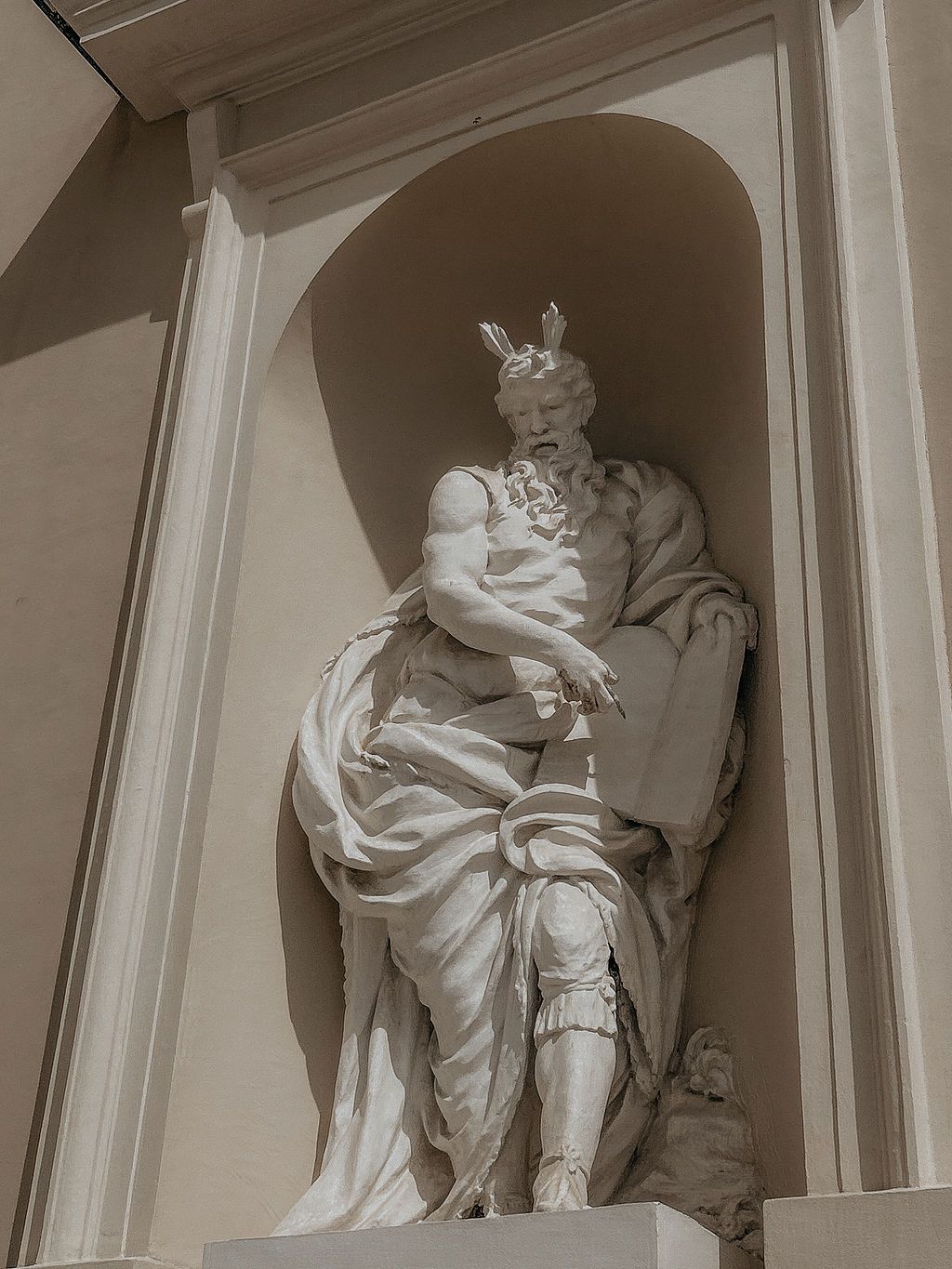 White marble statue of a robed classical figure wearing a crown, set in an architectural niche on a building facade.