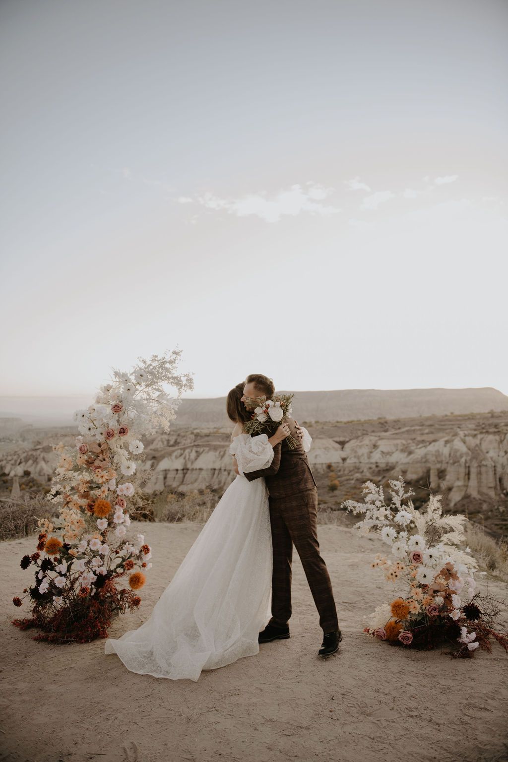 Couple sharing a first kiss at desert wedding ceremony with boho floral arrangements in Cappadocia, Turkey.