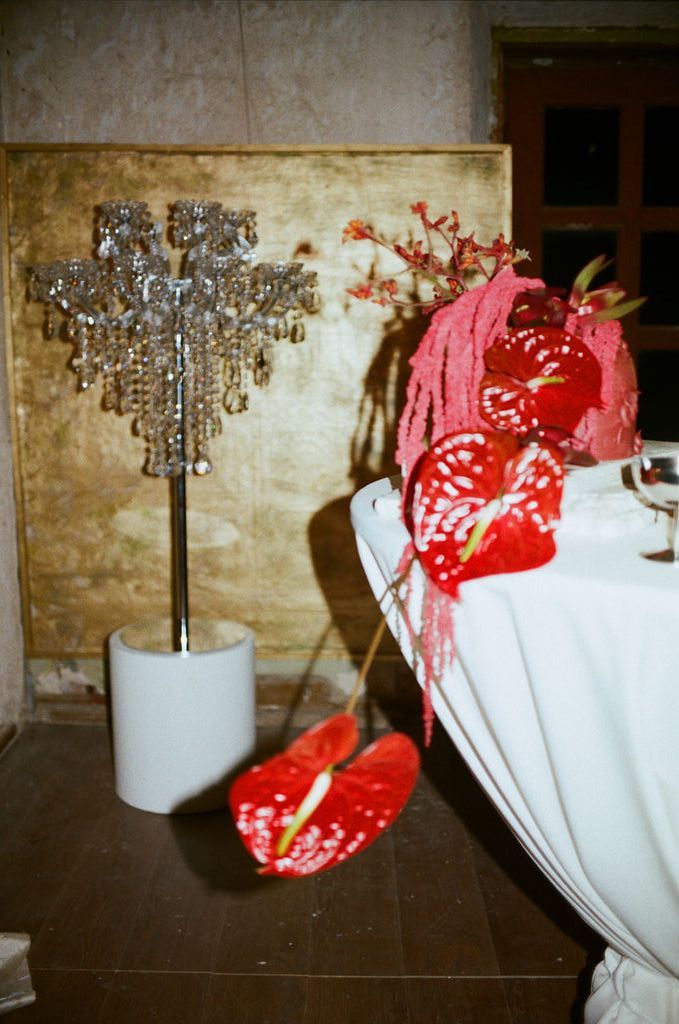 Crystal candelabra centerpiece beside red anthurium flowers on white draped table at elegant event.