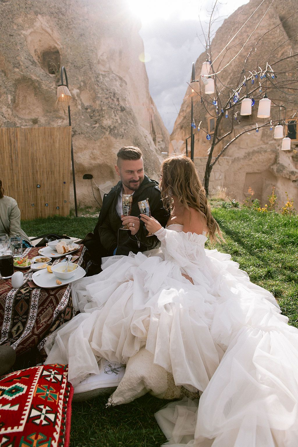 A bride and groom toast with champagne at an outdoor wedding reception in Cappadocia, Turkey, surrounded by cave rocks.