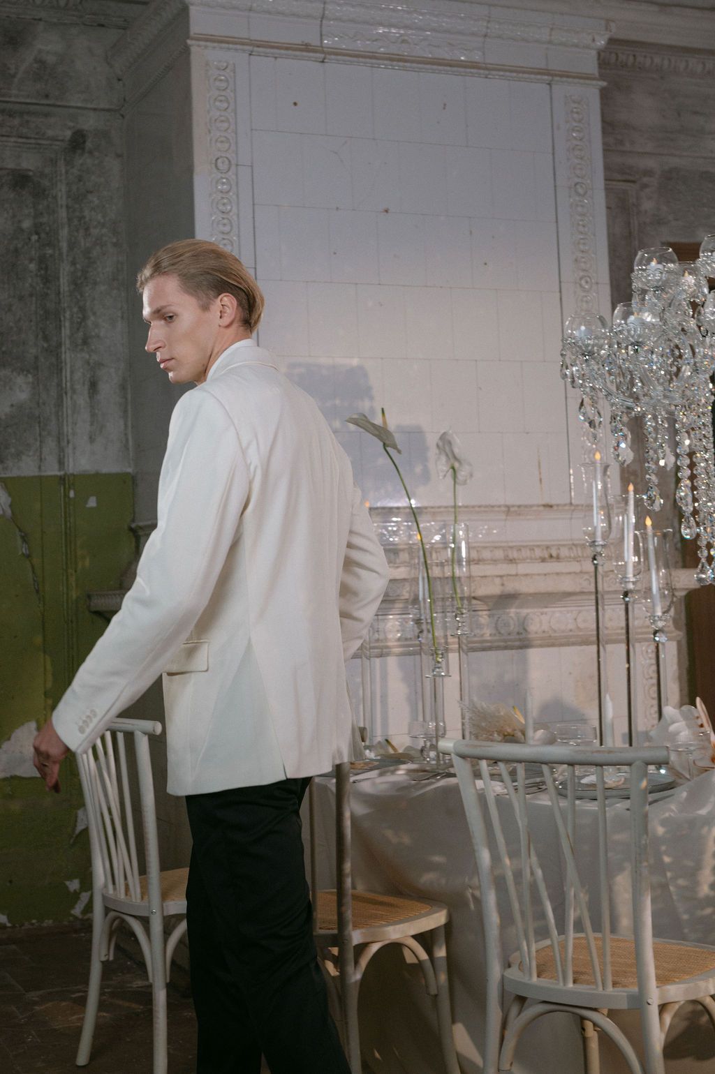Man in white jacket viewed from behind standing near white chairs and crystal decor in vintage venue.