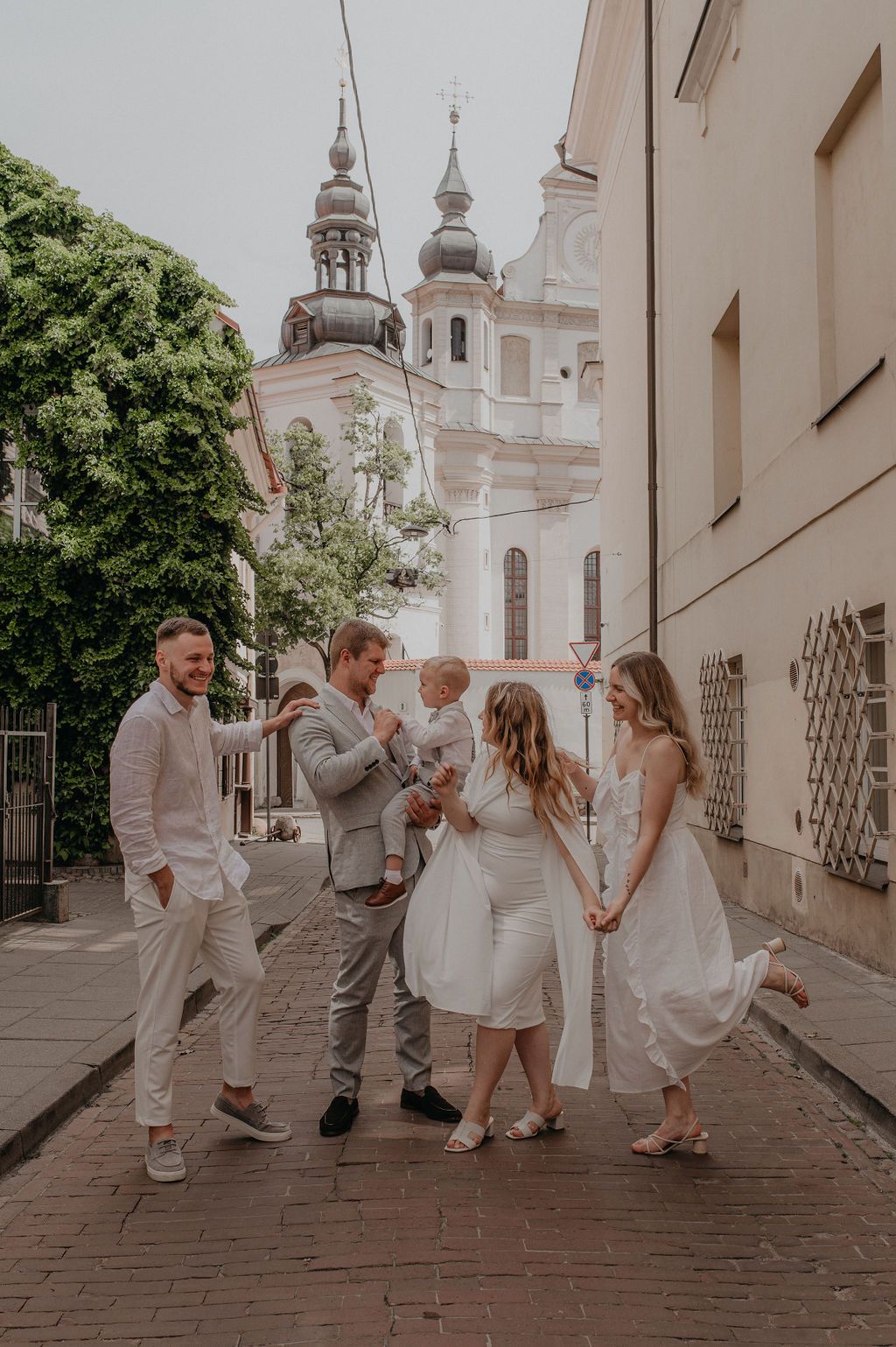 Family group in white outfits celebrating outdoors near historic church towers in European old town street.