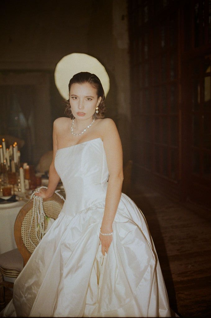 Bride in white strapless ball gown with halo headpiece and pearl necklace poses by candlelight.