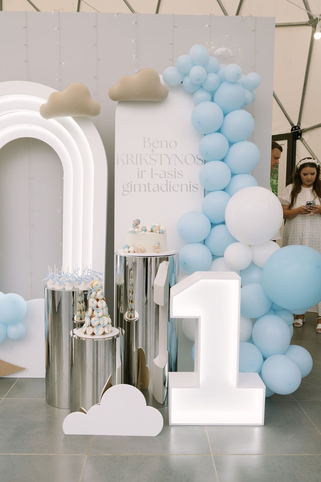 Baby boy's first birthday party decor with blue balloons, number 1, cloud props, and silver dessert stands.