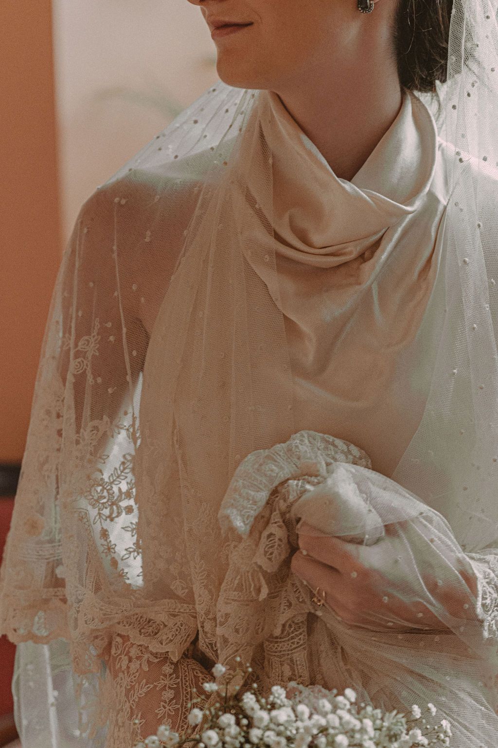 Bride in elegant lace wedding dress with pearl-dotted veil holding a delicate baby's breath bouquet.