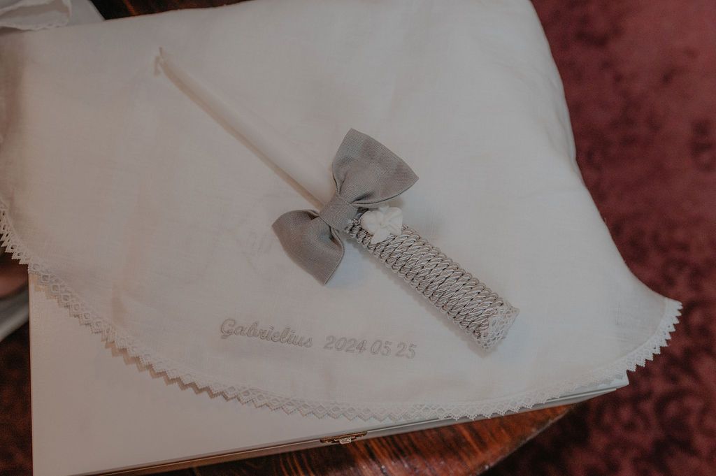 White baptism cloth with gray bow candle and embroidered name Gabriellius dated 2024.05.25.