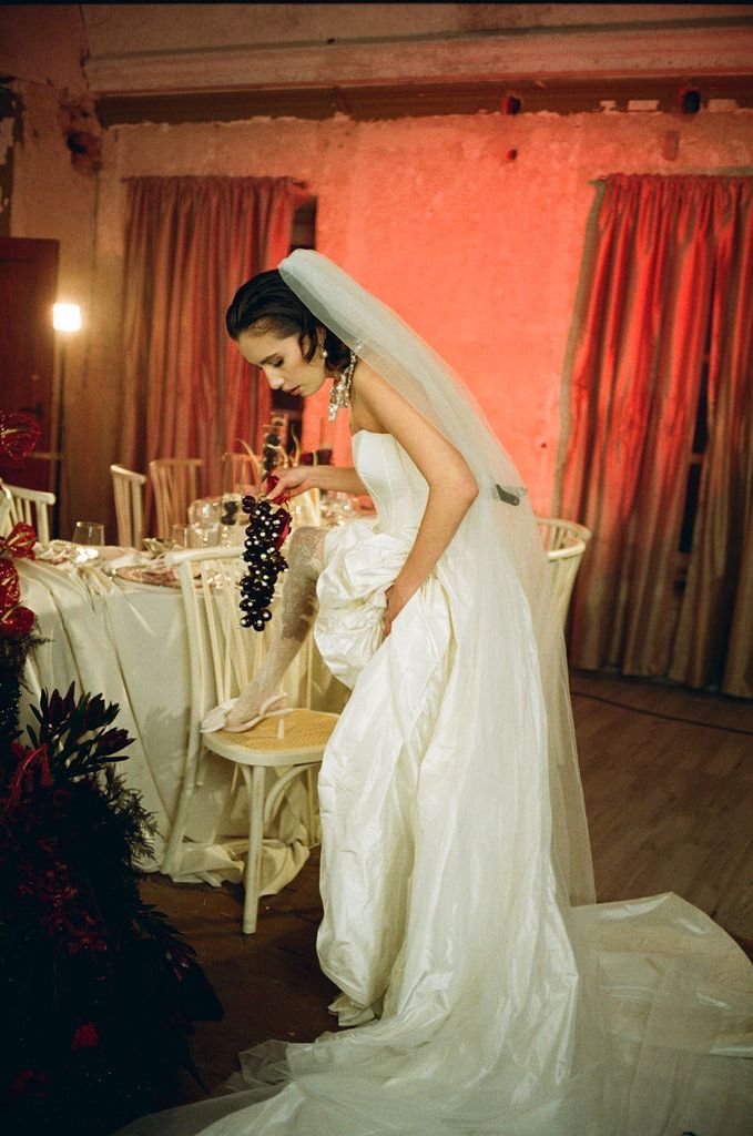 Elegant bride in white strapless wedding gown with veil standing by decorated reception table in warmly lit venue.