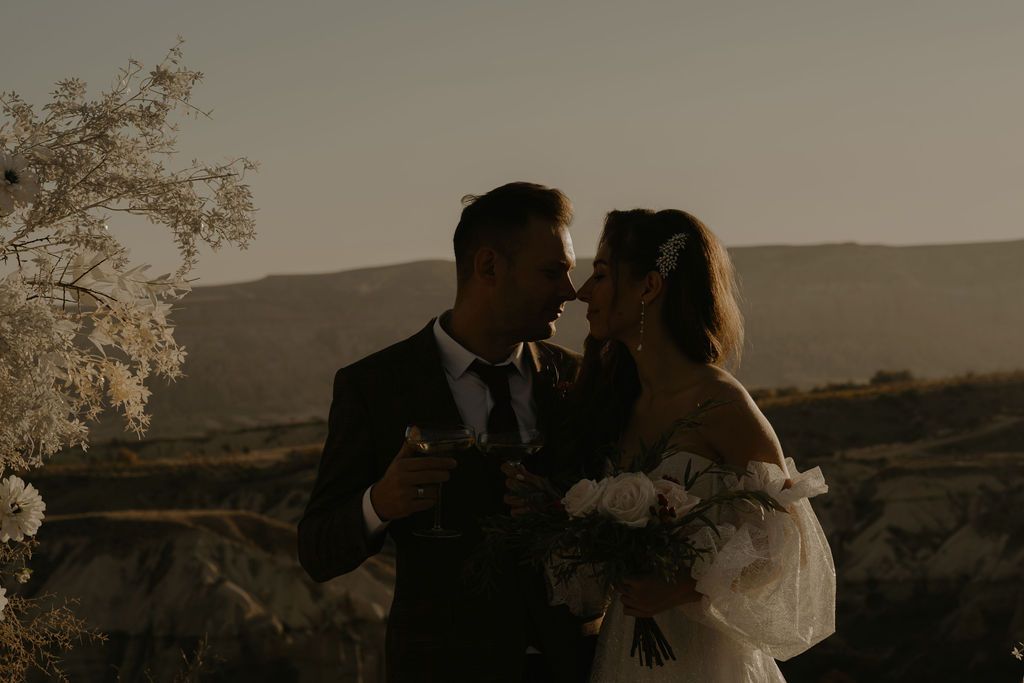 Bride and groom share a romantic moment at sunset with scenic mountain landscape in background at outdoor wedding.